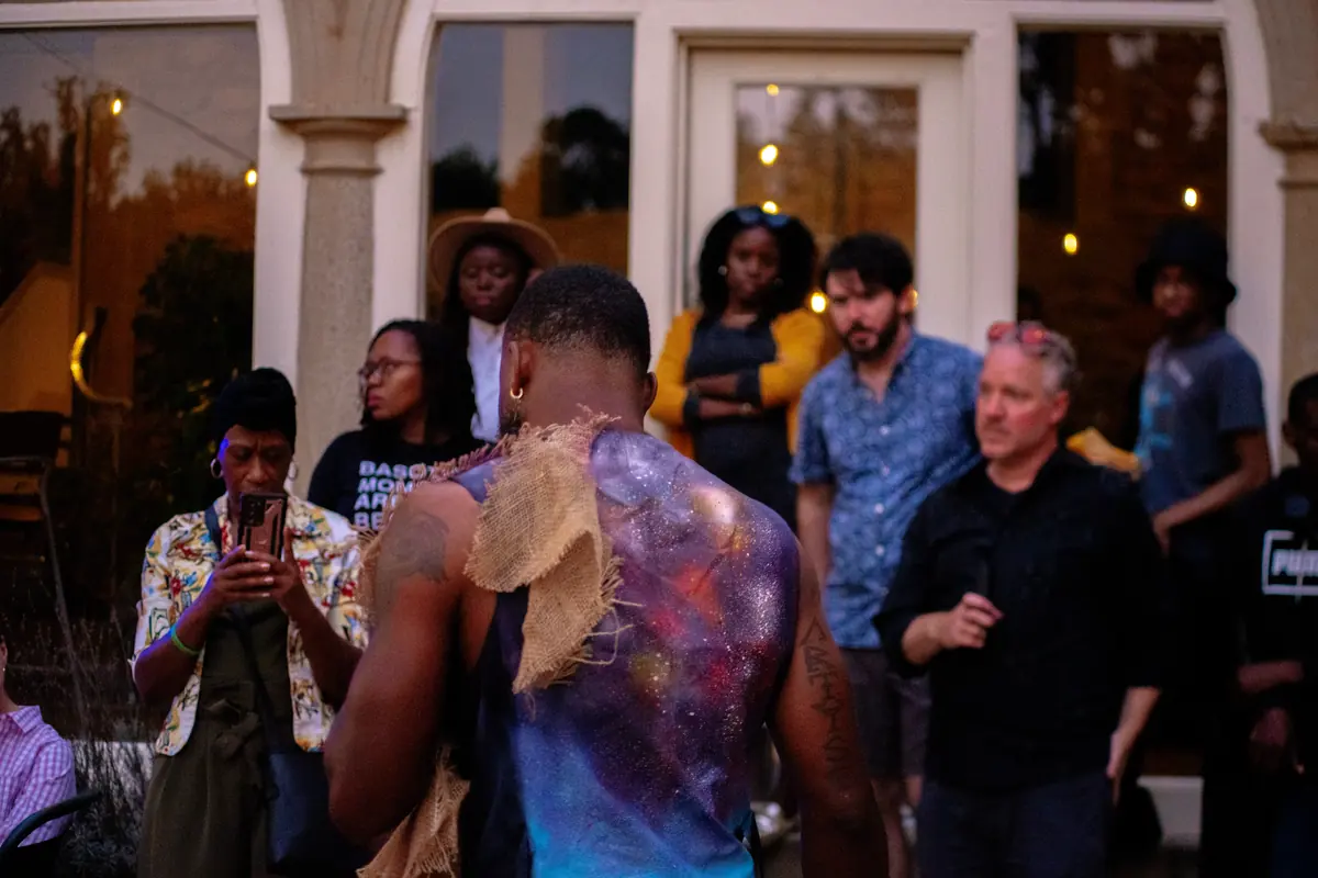 An outdoor crowd gathered around a body-painted performer at an evening event
