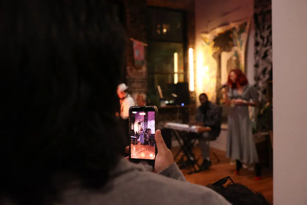 A guest filming a live performance on a phone at an evening art event