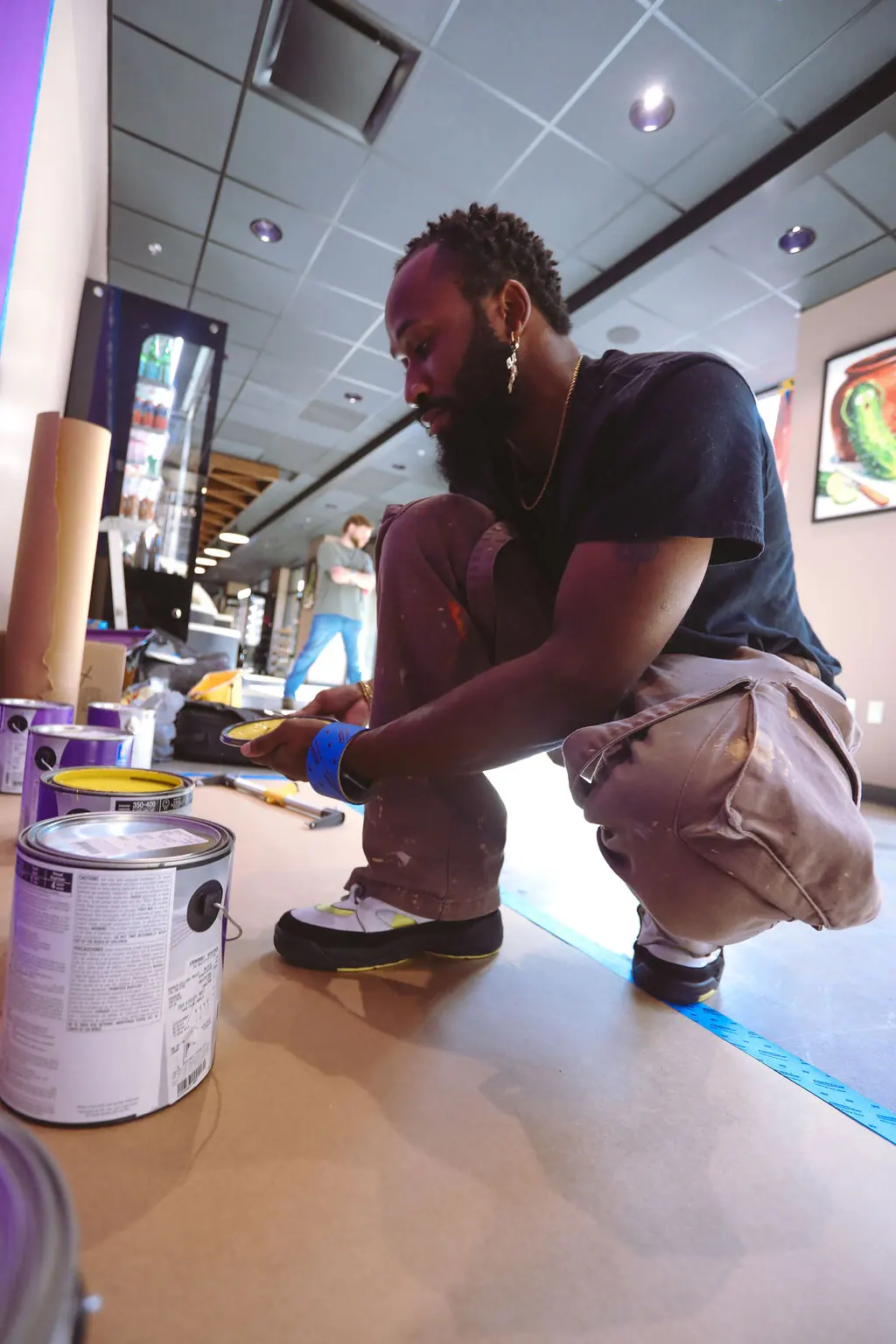 Micah The Artyst crouched among paint cans, preparing a large work on the floor