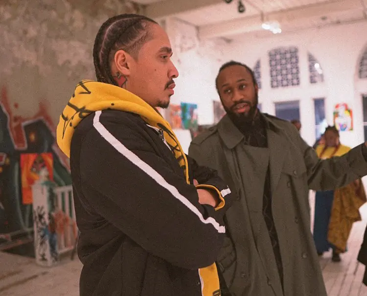 Micah The Artyst in conversation with a guest among murals at an exhibition