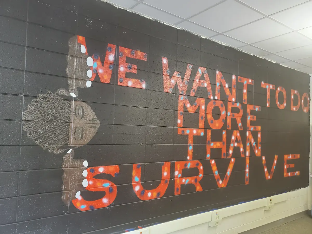 A large wall work reading We want to do more than survive, in a bright public interior