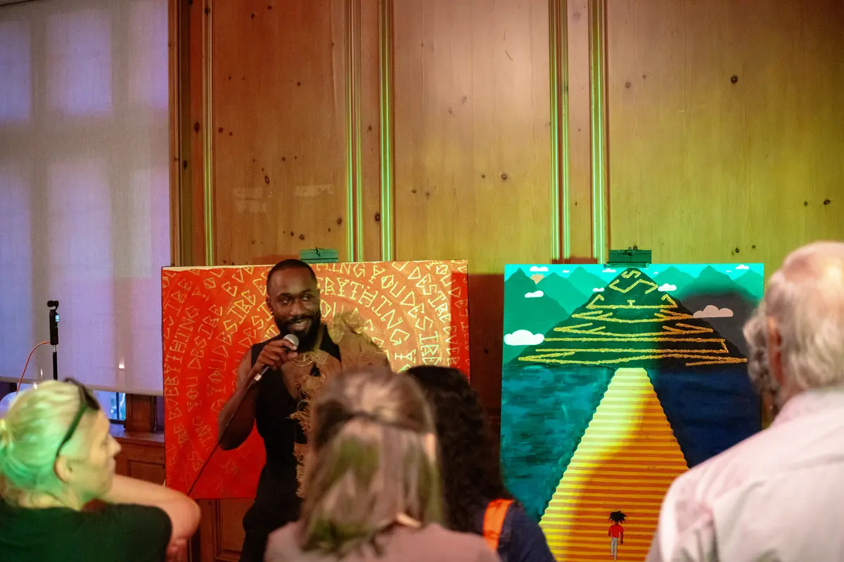 Micah The Artyst speaking to guests beside his paintings at an exhibition
